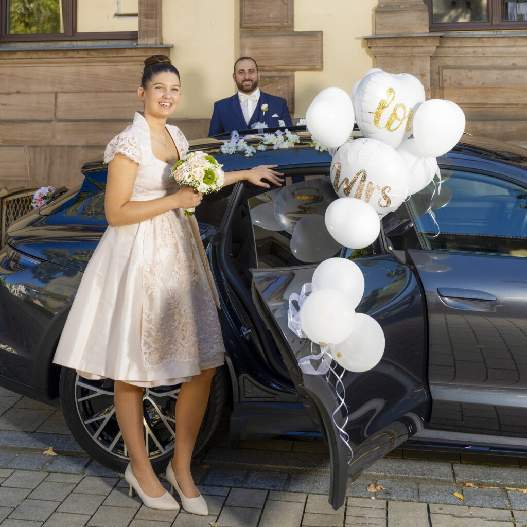 Hochzeitsbild Erlangen-Schlosspark.
Das Brautpaar posiert vergnügt  und ganz verliebt vor dem Hochzeitsauto.