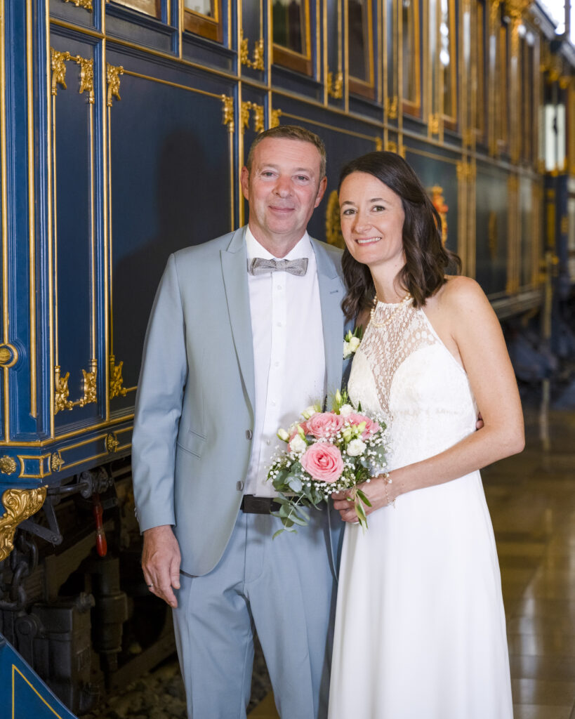 Hochzeitsfoto im DB Museum Nürnberg.
Das Brautpaar steht vor einem blauen Eisenbahnwagen.