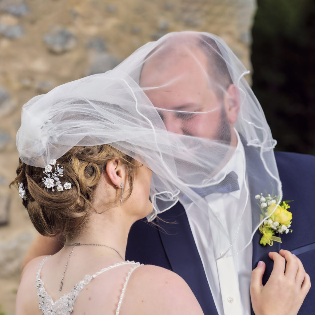 Das Hochzeitspaar küsst sich  verdeckt unter dem Brautschleier.